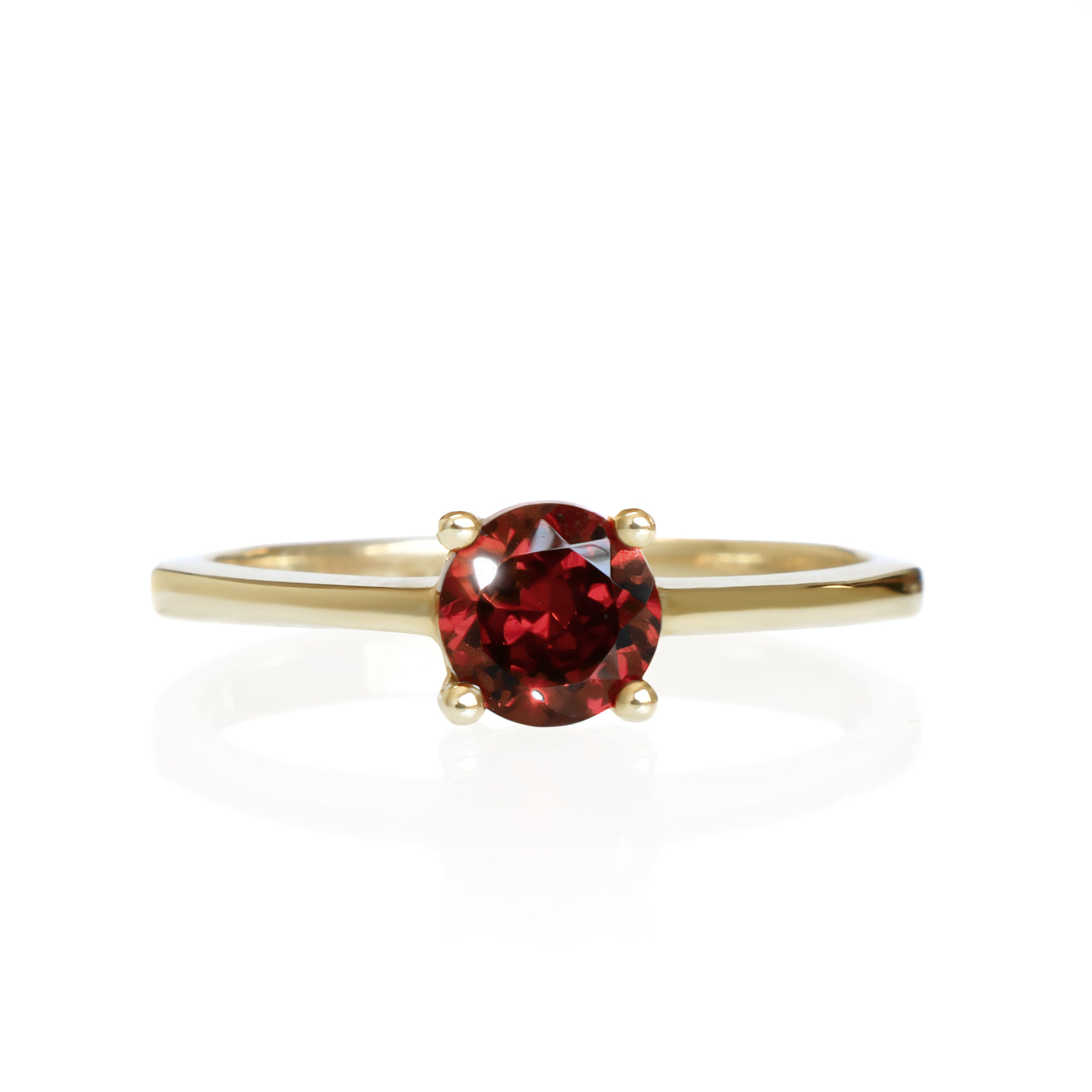 A product photo of a Round Garnet Solitaire Ring in 9k Yellow Gold sitting on a plain white background. The garnet centre stone measures 5.5mm. The stones are a deep red, reflecting sanguine hues across their multi-faceted edges.