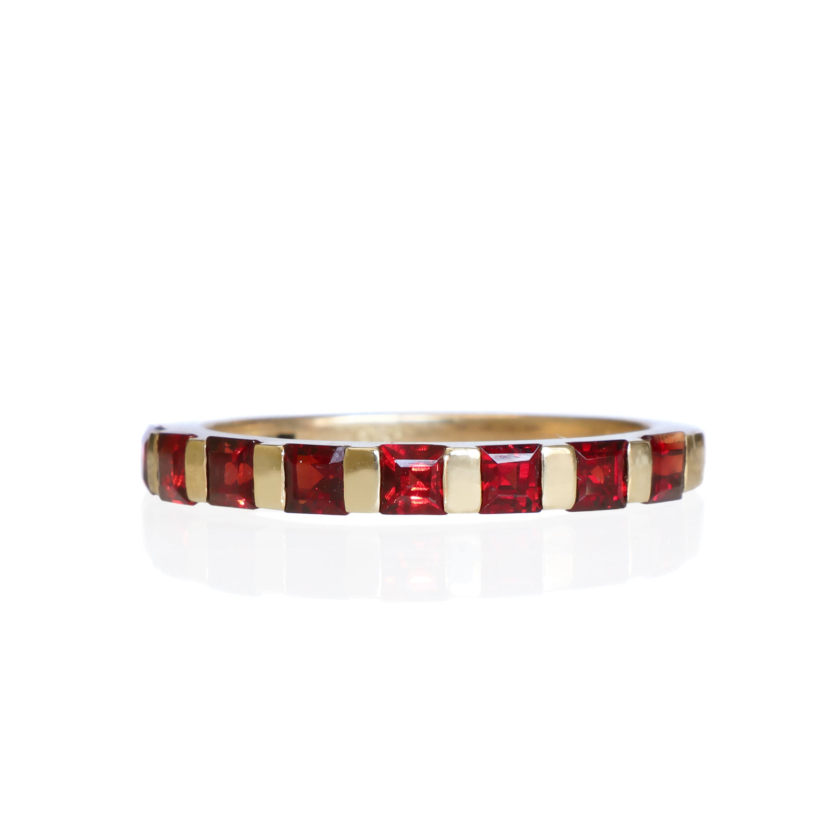 A product photo of a Multi-Square Garnet Ring in 9k Yellow Gold sitting on a plain white background. The 8 garnet stones measure 2.5mm across and are deep red, reflecting sanguine hues across their multi-faceted edges.