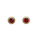 A product photo of 4mm Round Bezel-Set Garnet Earring Studs in 9k Yellow Gold sitting on a plain white background. The 2 garnet stones measure 4mm across and are deep red, reflecting sanguine hues across their multi-faceted edges, framed in a thick layer of yellow gold.