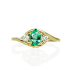 A product photo of a mystical tsavorite and diamond fantasy ring in solid 9k yellow gold on a white background. The deep, verdant-green tsavorite is held in place by 4 claws and reflects light off of its many facets, while the diamonds on either side are held by 3 each. The smooth yellow gold band curves elegantly, meeting at the top and bottom of the tsavorite and diamond arrangement.