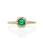 A product photo of a classic diamond halo emerald ring in solid 9k yellow gold on a white background. The rounded band is smooth and minimalistic. The deep, mint-green emerald centre stone is held in place by 6 claws and reflects light off of its many facets.