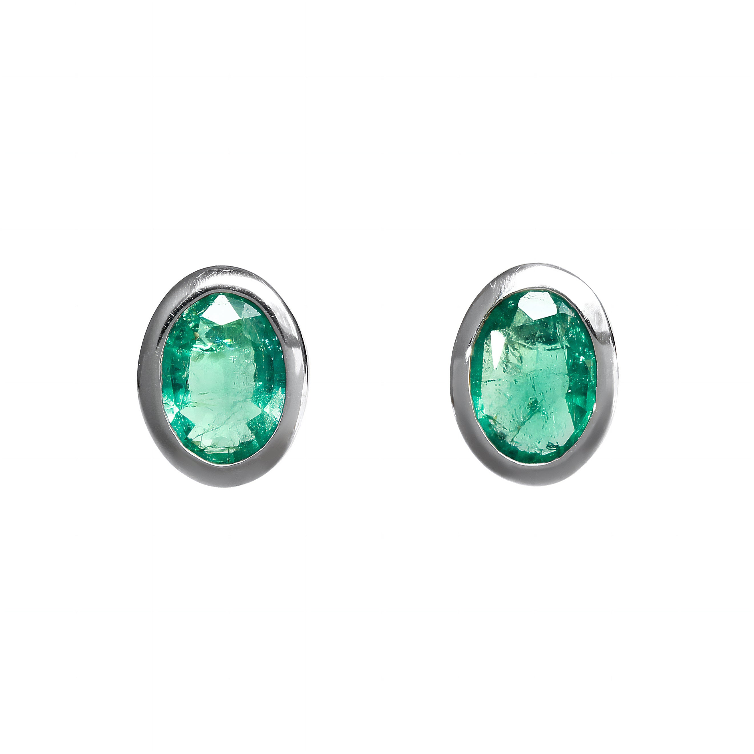 A product photo of a pair of fine emerald earrings in 9k white gold sitting on a white background. The fine 7x5mm fine emeralds are framed in a thick layer of white gold in a bezel setting.