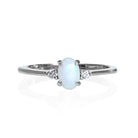 A product photo of a delicate 9ct white gold 6x4mm white opal and diamond trio ring sitting on a white background. The fiery opal centre stone is hugged on either side by a bright white diamond jewel.