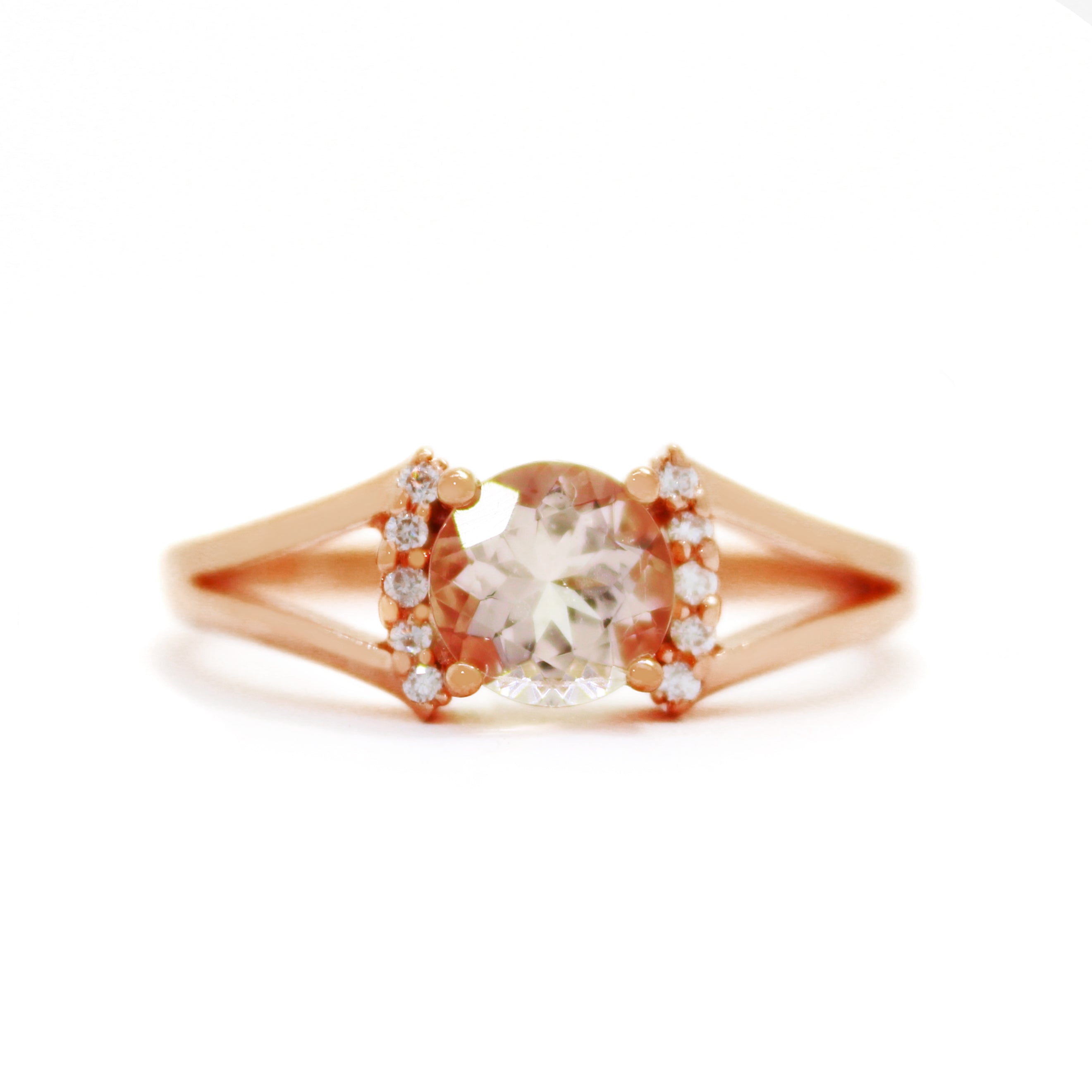 A product photo of a sophisticated pale pink morganite split-band ring with diamond framing sitting on a white background. 4 diamonds sit on either side of the morganite gemstone, with the rose gold split band on either side holding the jewel and diamond arrangement in place.