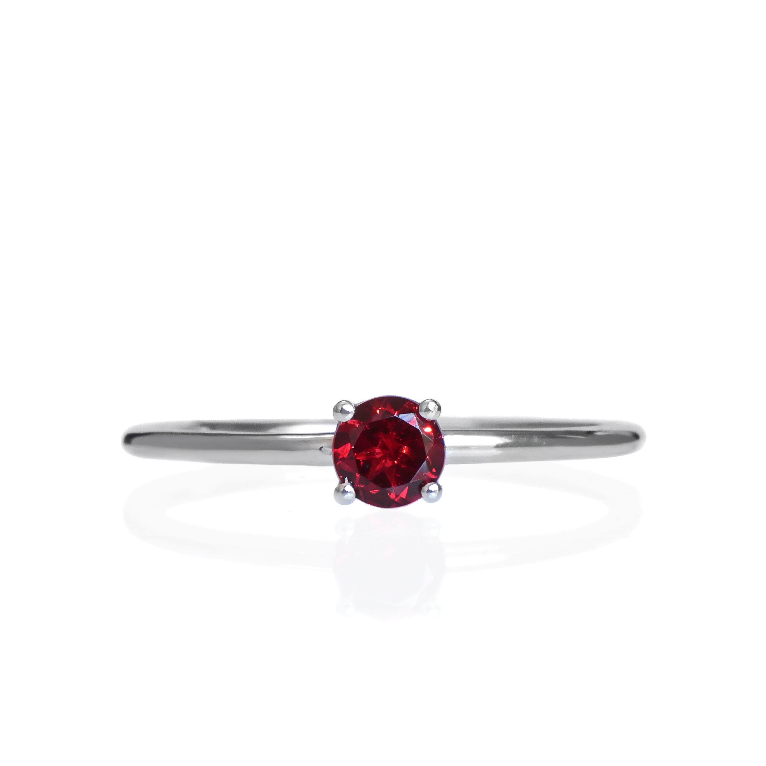 A product photo of a delicate white gold stacking ring with a tiny, claw-set garnet in the centre sitting on a white background. The band is slim and thread-like, with the focus drawn to the petite 4mm glinting garnet gemstone.