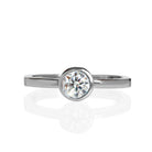 A product photo of a solid 925 sterling silver bezel-set solitaire ring. A single, dazzling white moissanite sits encased in a thick layer of silver framing. The white colouring and multi-coloured refractions would make it a good diamond alternative.