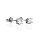 A product photo of a pair of 9 karat white gold lab diamond stud earrings sitting in the sun on a white textured background. The brilliant, colourless half pointer round diamonds measure 5mm across, and are held in place by a simple 4-claw setting.