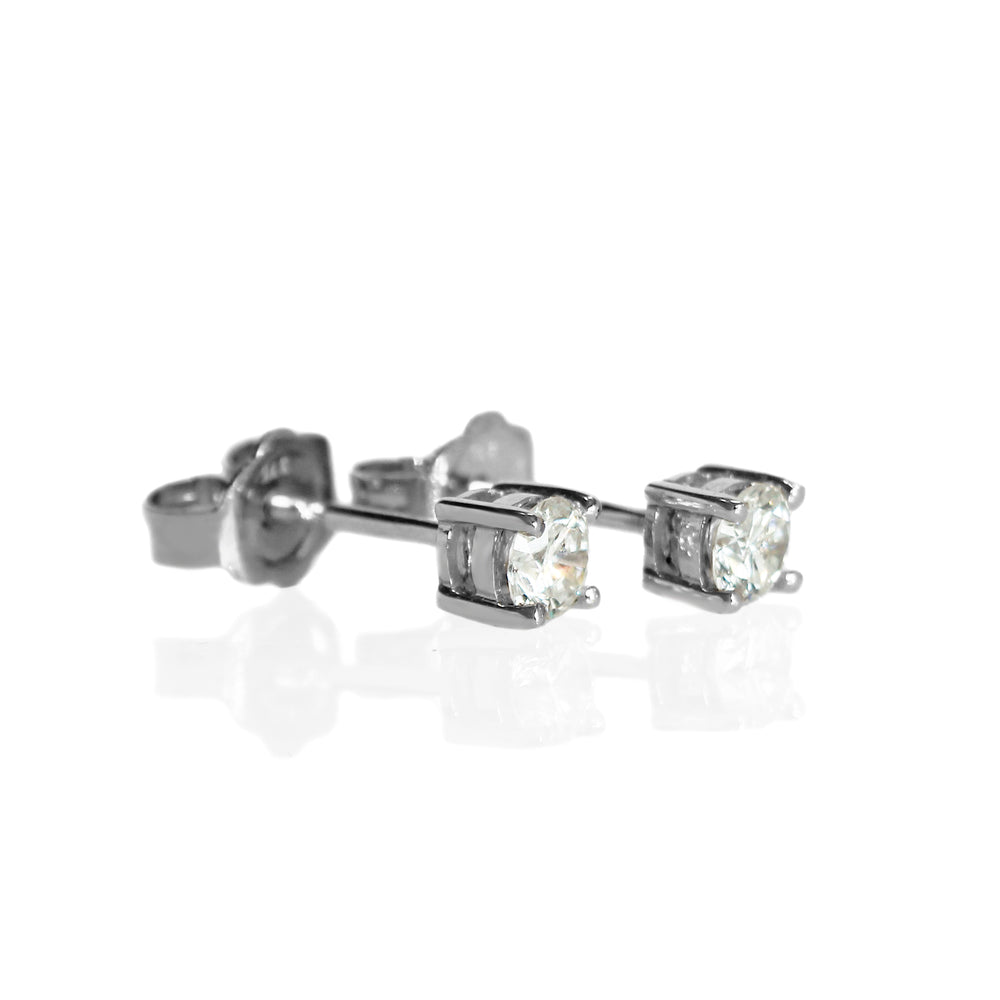 A product photo of a pair of 9 karat white gold lab diamond stud earrings sitting in the sun on a white textured background. The brilliant, colourless half pointer round diamonds measure 4mm across, and are held in place by a simple 4-claw setting.