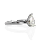 A product photo of a 14 karat white gold lab diamond solitaire engagement ring sitting in the sun on a white textured background. The brilliant, colourless 1 carat pear-cut diamond measures 8.73mm lengthwise, and is held in place by 3 delicate claws in a high-profile cathedral setting in the middle of a tapered band.