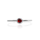 A product photo of a delicate silver stacking ring with a tiny, bezel-set garnet in the centre sitting on a white background. The band is slim and thread-like, with the focus drawn to the petite 3mm glinting red centre stone. The deep red gemstone colour would be a good ruby alternative.