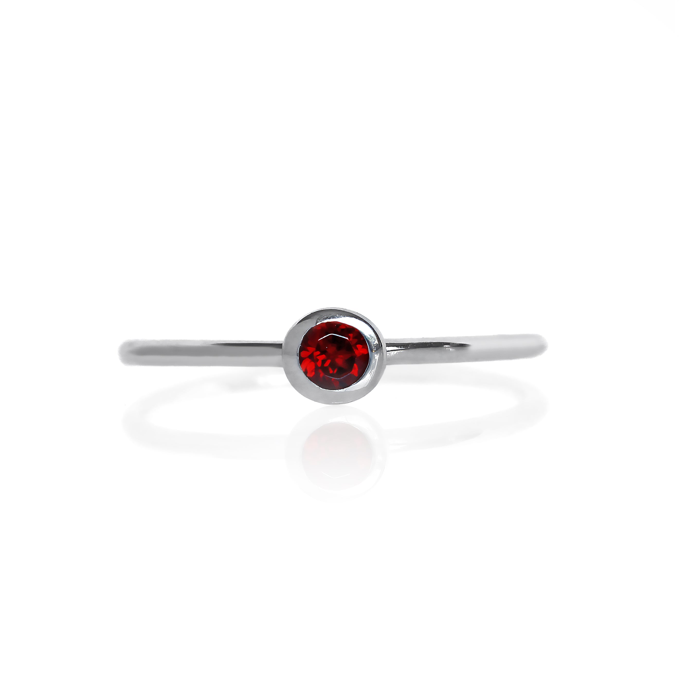 A product photo of a delicate silver stacking ring with a tiny, bezel-set garnet in the centre sitting on a white background. The band is slim and thread-like, with the focus drawn to the petite 3mm glinting red centre stone. The deep red gemstone colour would be a good ruby alternative.