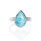 A product photo of a silver Larimar ring on a white background. The band is tall and thick. The 14x9mm pear cabochon Larimar stone has dappled white and light blue patterning, similar to water reflections at the bottom of a pool. The stone is set in a thick silver bezel setting.