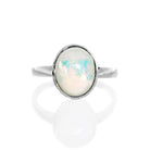 A product photo of a silver rainbow opal ring on a white background. The band is tall and thick. The 10x8mm oval cabochon opal stone is uniquely translucent, with a moonstone-like sheen and rainbow-coloured fire. The stone is set in a thick silver bezel setting.