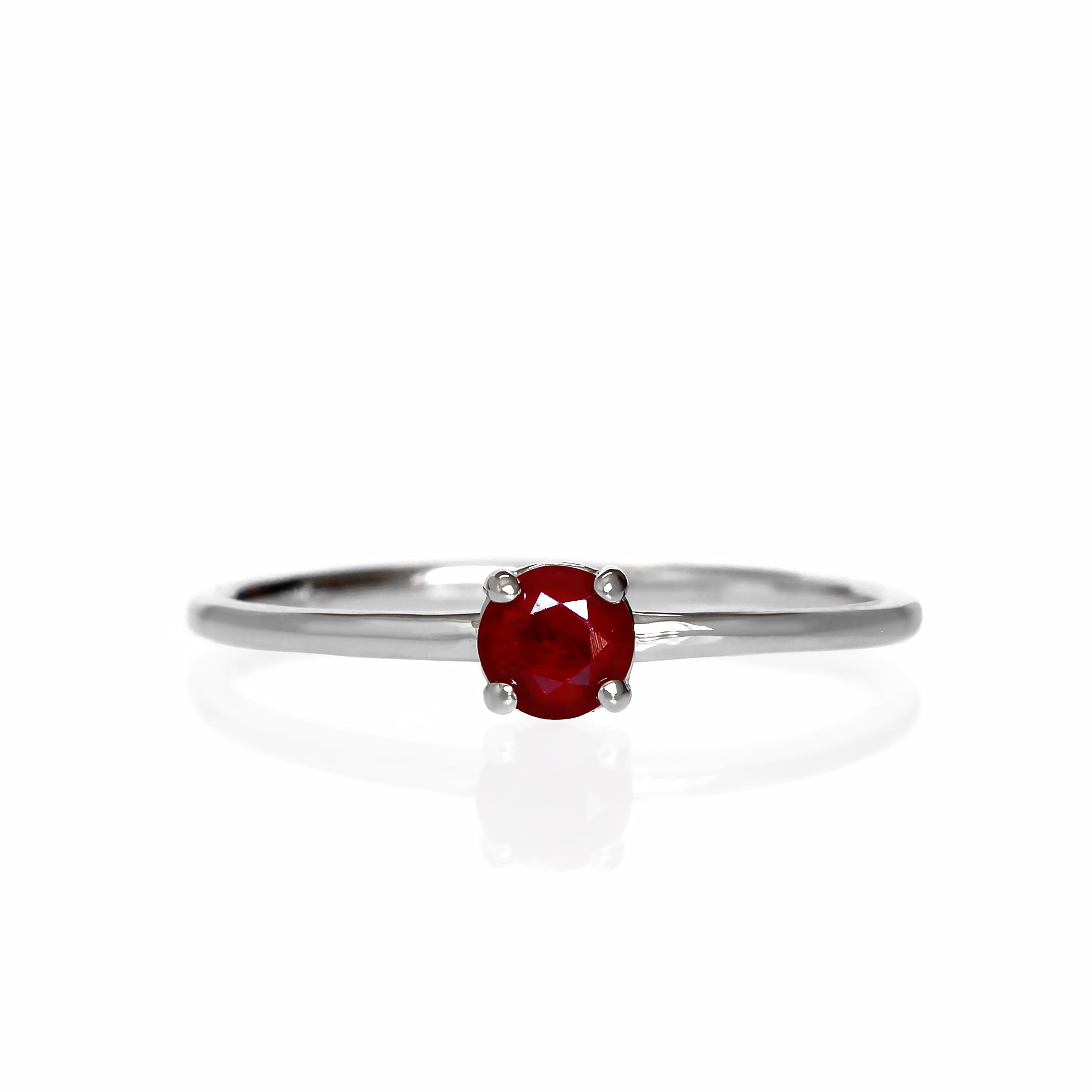 A product photo of a delicate white gold stacking ring with a tiny, claw-set ruby in the centre sitting on a white background. The band is slim and thread-like, with the focus drawn to the petite 4mm glinting burgundy red gemstone.