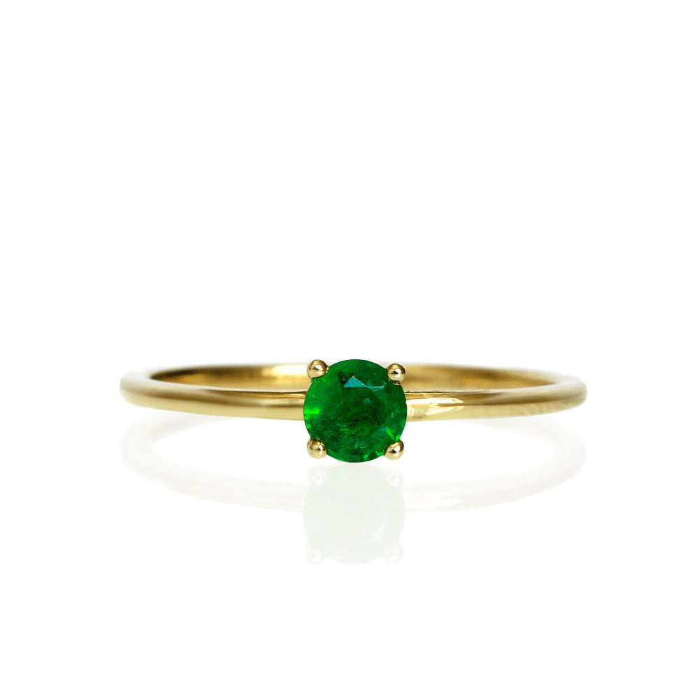 A product photo of a delicate yellow gold stacking ring with a tiny, claw-set emerald in the centre sitting on a white background. The band is slim and thread-like, with the focus drawn to the petite 4mm glinting green emerald gemstone.