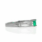 A product photo of a modern emerald ring made of solid 9k white gold sitting on a white background. The 4mm square-shaped emerald is held in place by 3 separate prongs, splitting apart from the back of the band.