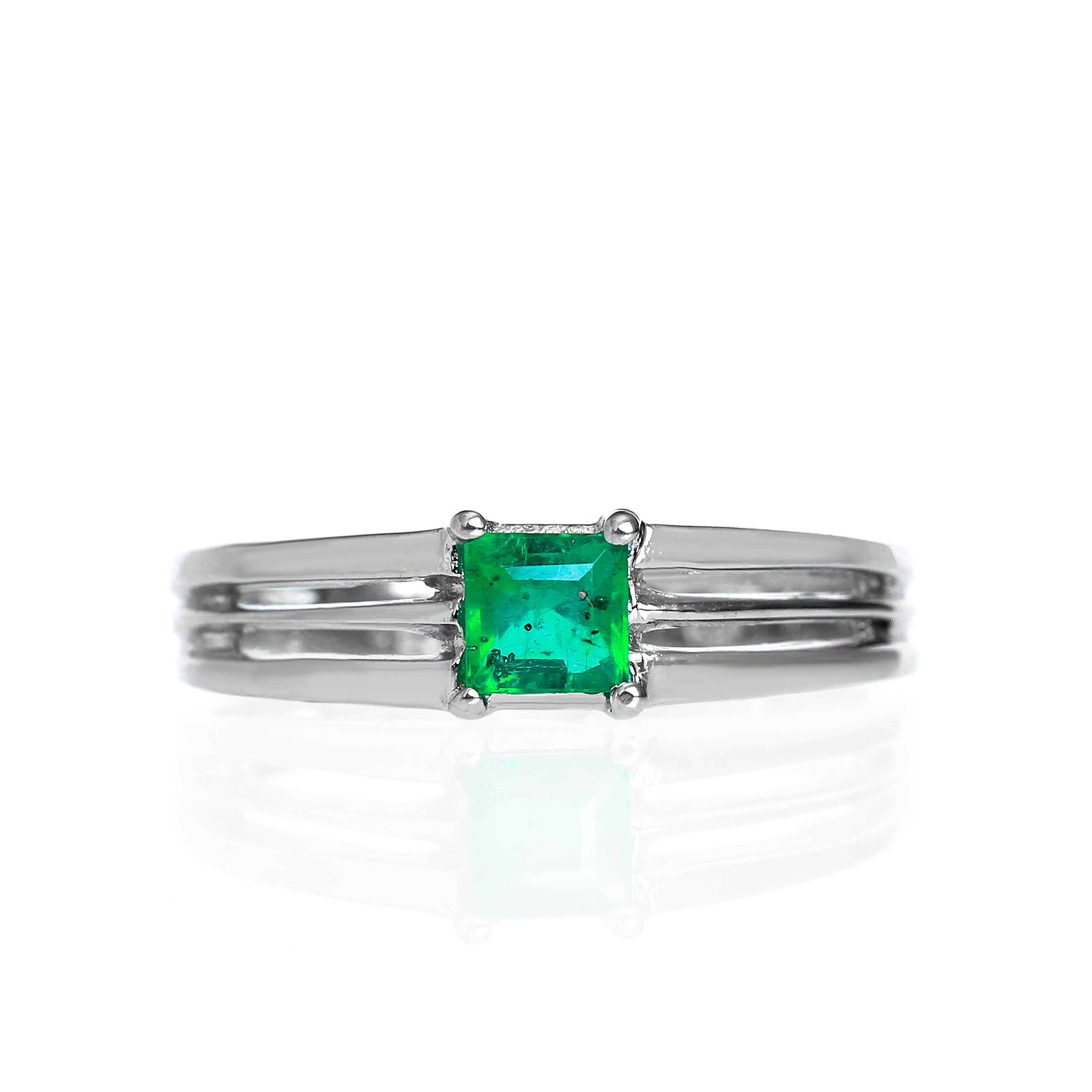 A product photo of a modern emerald ring made of solid 9k white gold sitting on a white background. The 4mm square-shaped emerald is held in place by 3 seperate prongs, splitting apart from the back of the band.