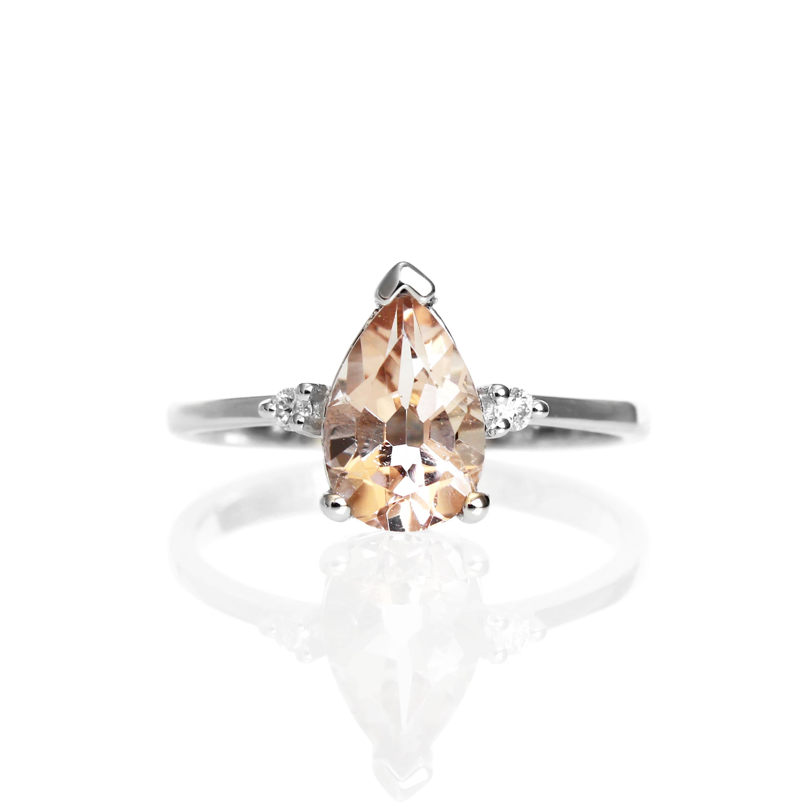 A product photo of a 9 karat white gold ring with a pear-cut peachy pink morganite centre stone sitting on a white background. The golden band is simple and smooth, meeting elegantly on either side of the morganite centre stone, hugged by a single diamond on either side.