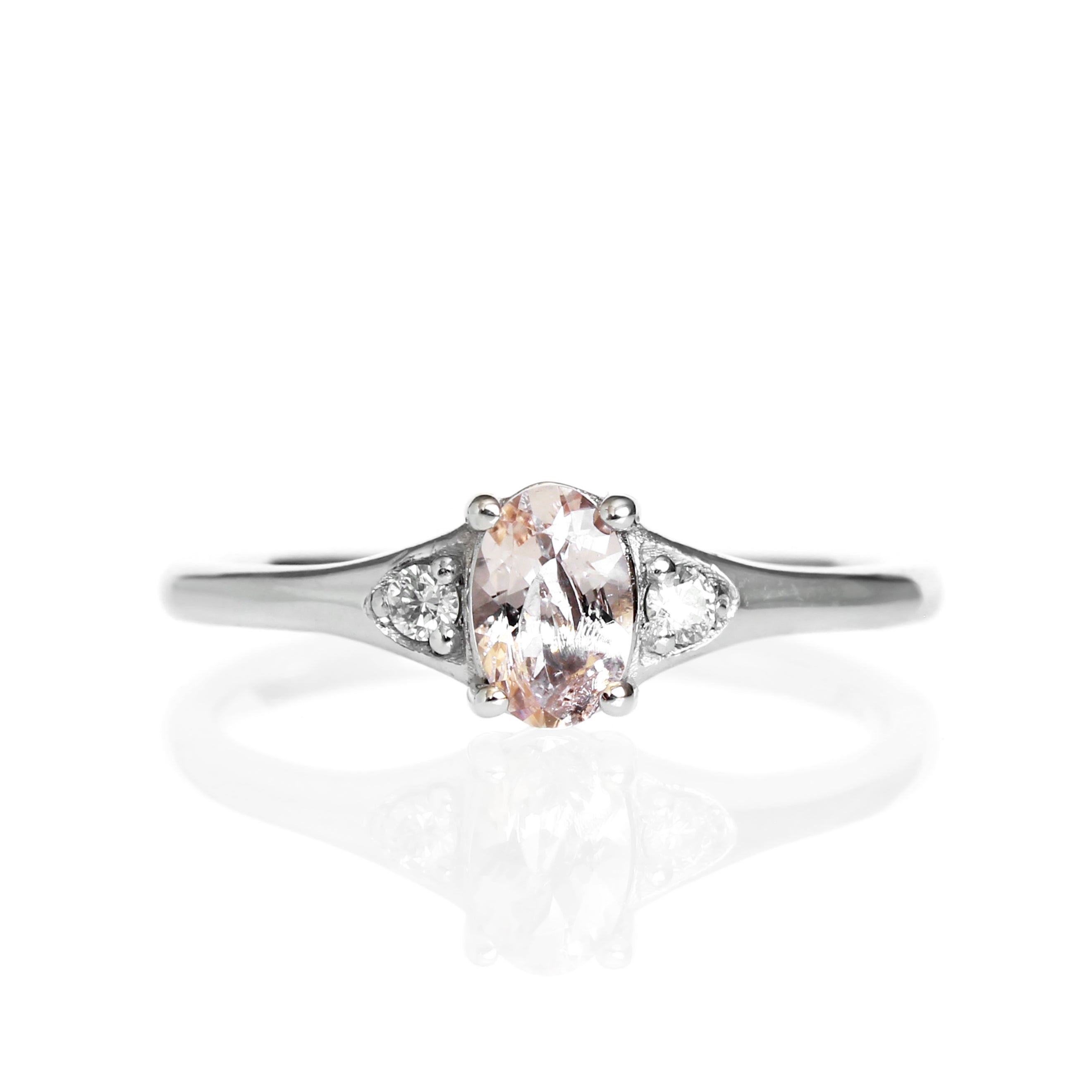 A product photo of a 9 karat white gold ring with an oval-cut pale pink morganite centre stone sitting on a white background. The golden band is simple and smooth, thickening closer to the face of the ring, framing the 6x4mm morganite stone and diamonds.