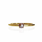 A product photo of a delicate yellow gold stacking ring with a tiny, claw-set greyish rosaline seed pearl in the centre sitting on a white background. The band is slim and thread-like, with the focus drawn to the petite 3mm opalescent pearl.