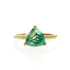 A product photo of a gold moss agate solitaire ring on a white background. The band is plain and smooth, meeting on either side of the 8mm trilliant faceted-cut moss agate gemstone, held in place by 3 delicate golden claws on each corner.