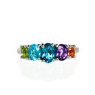 A product photo of a multi-gemstone stacking ring, featuring various birthstones of smalller sizes getting increasingly bigger towards the central 6x4mm oval London Blue topaz jewel.