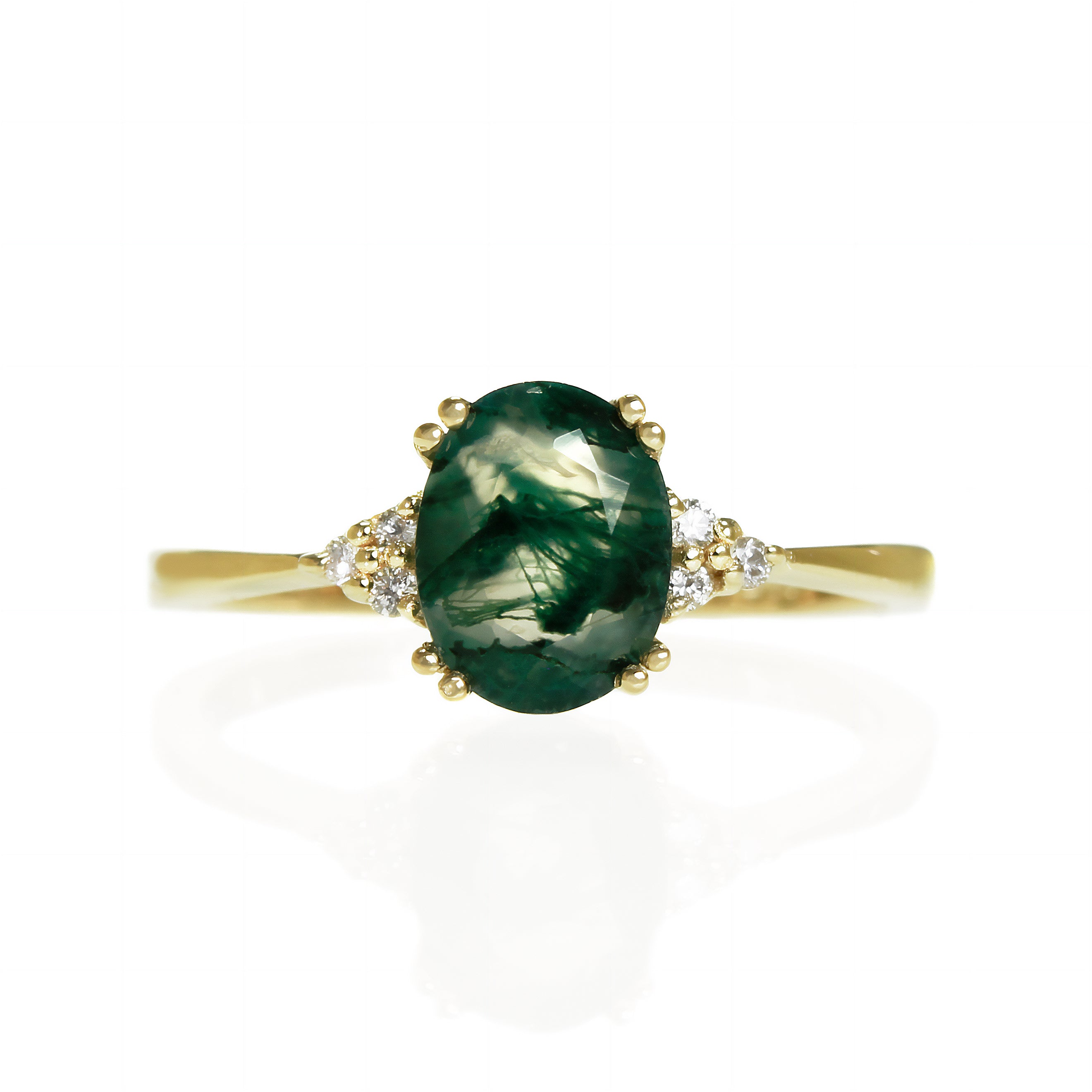 A product photo of a yellow gold moss agate and diamond trio ring sitting on a white background. The oval, naturally-included moss agate gemstone stands in stark contrast to the little clusters of three classic white diamond stones on either side.