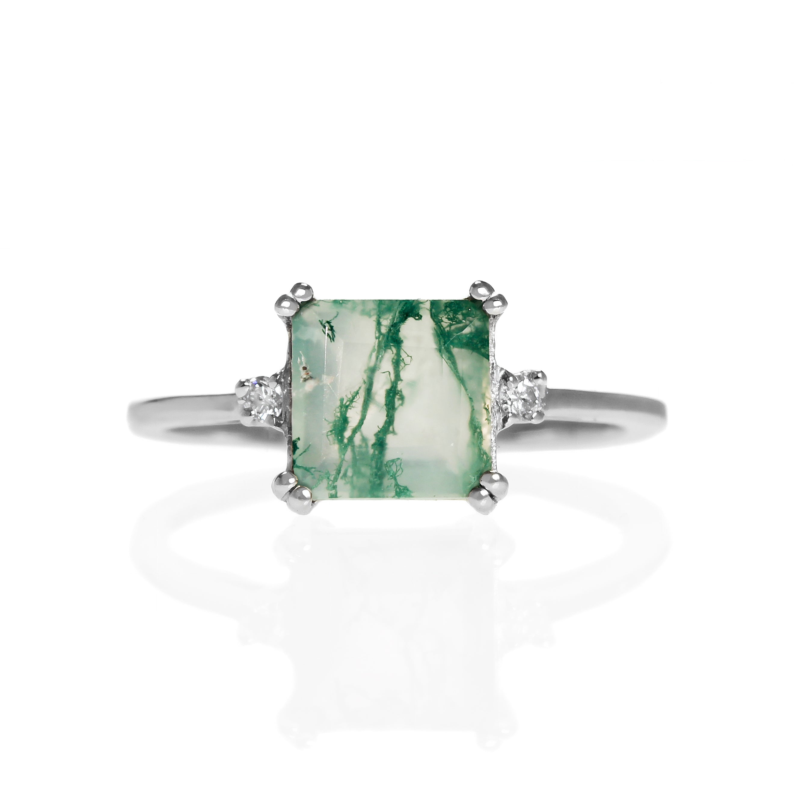 A product photo of a 7x7mm square cut moss agate and diamond ring on a white background. The ring is made of solid 9 karat white gold, with a smooth band and double-clawed settings on each corner of the moss agate centre stone - holding it in place. On either side of the stone is a 0.02ct natural diamond, held in place by 4 delicate golden prongs.