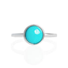 A product photo of a turquoise silver solitaire ring on a white background. The ring consists of a singular 7mm round cabochon-cut gem encased in a layer of silver bezel setting. The blue turquoise stone hails straight from the Sleeping Beauty mountains of Arizona. The band is simple and smooth silver metal. 