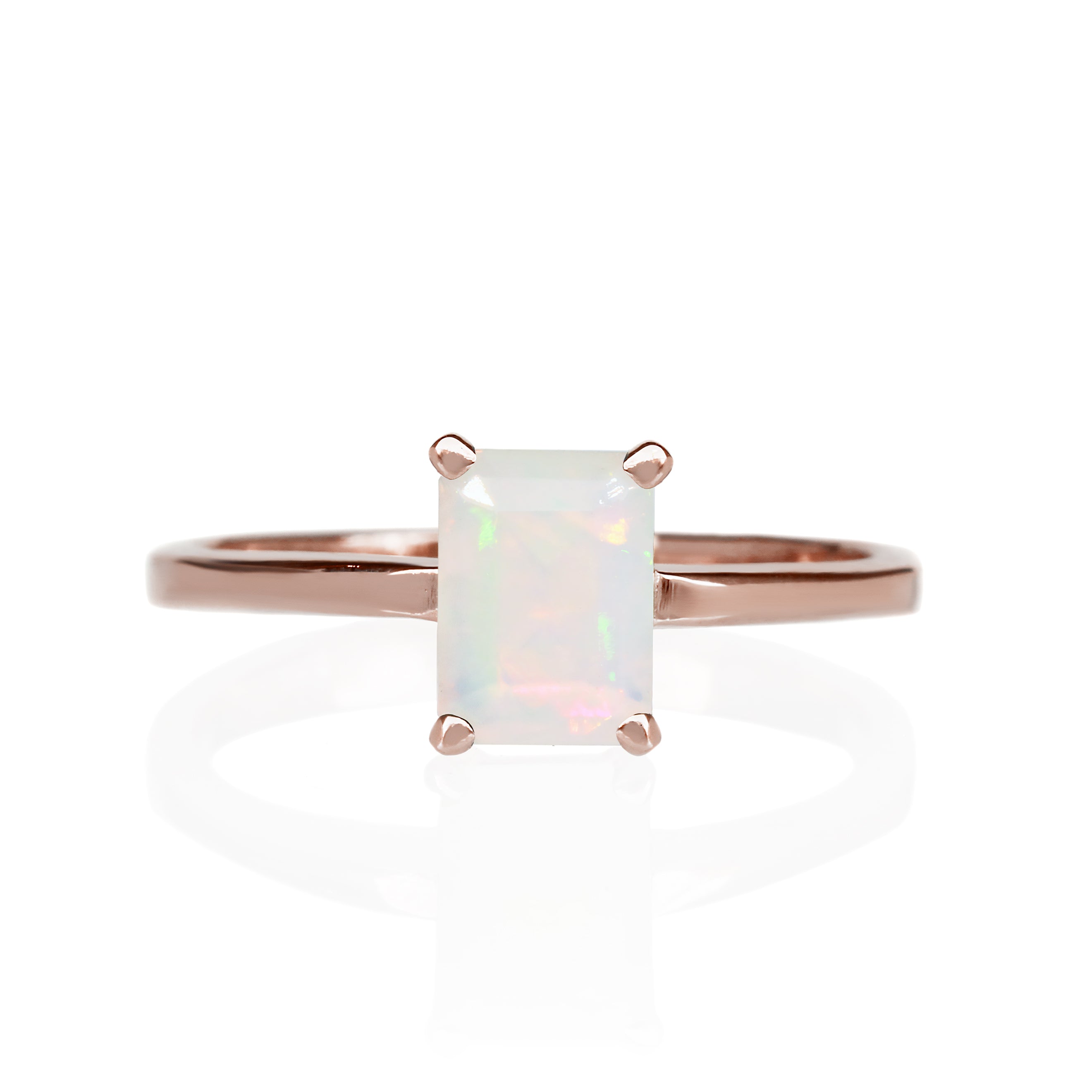 A product photo of a rainbow opal solitaire ring in solid 9 karat rose gold sitting on a white background. The band is simple and smooth. On the face of the ring is a vertically-oriented 7x5mm rectangular gemstone, held in place by 4 golden claws. 