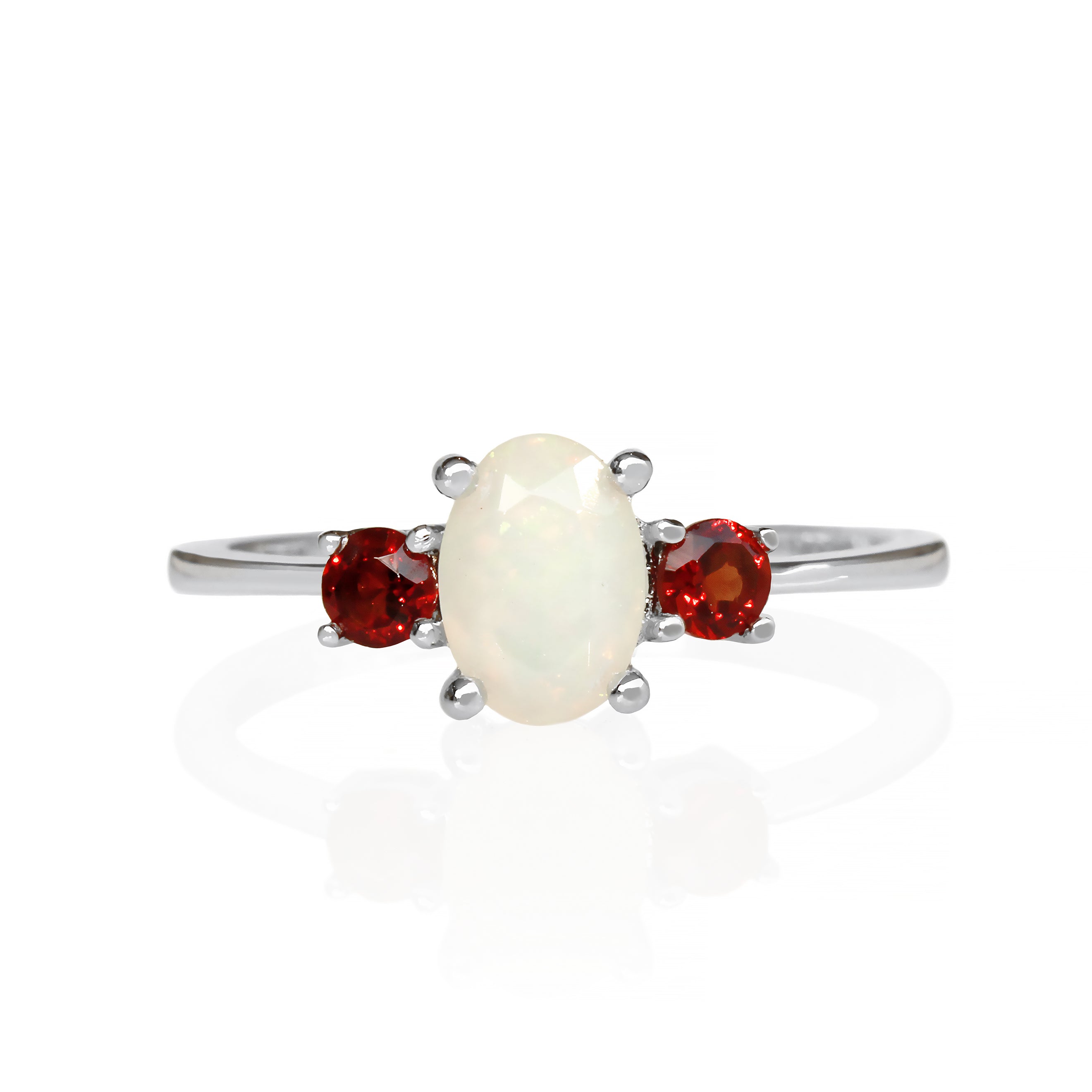 A product photo of a faceted rainbow opal and garnet ring in 9 karat white gold on a white background. The faceted cut of the opal allows the viewer to observe the rainbow-hued fire within, while the red garnet sidestones contrast the softness of the centre stone.