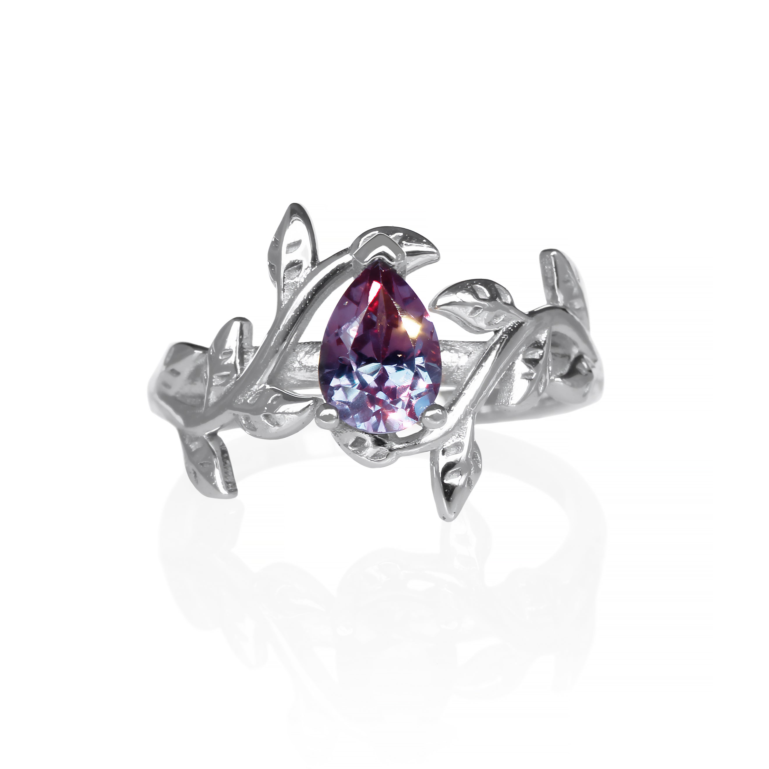 A product photo of a delicate and ornate sterling silver ring featuring a 7x5mm pear lab-grown alexandrite centre stone on a white background. The alexandrite stone displays a stunning range of colors, including deep purple and vibrant blue, depending on the lighting conditions. The ring's intricate floral band is adorned with delicate leaf-like motifs, meticulously crafted with detailed veins and edges. Ideal for use as a promise ring, this nature-inspired piece showcases the beauty of lab-grown gemstones 