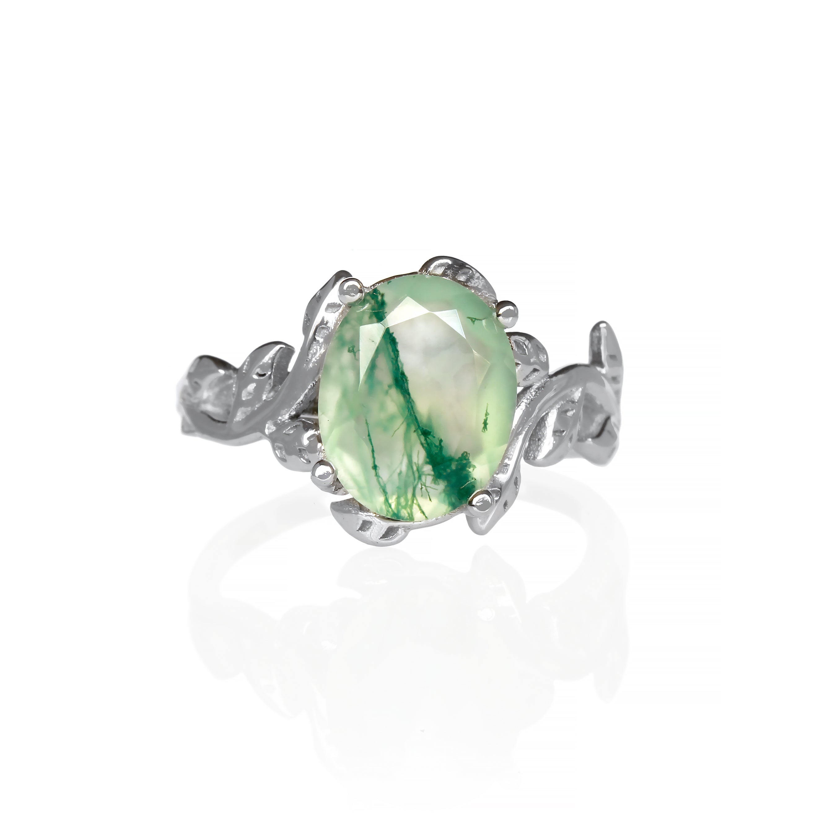 A delicate and ornate sterling silver ring featuring a 10x8mm oval moss agate center stone on a white background. The moss agate stone displays a unique pattern of green dendritic inclusions, resembling moss or lichen. The ring's intricate floral band is adorned with delicate leaf-like motifs, meticulously crafted with detailed veins and edges. Ideal for use as a promise ring, this nature-inspired piece showcases the beauty of natural gemstones and intricate craftsmanship.