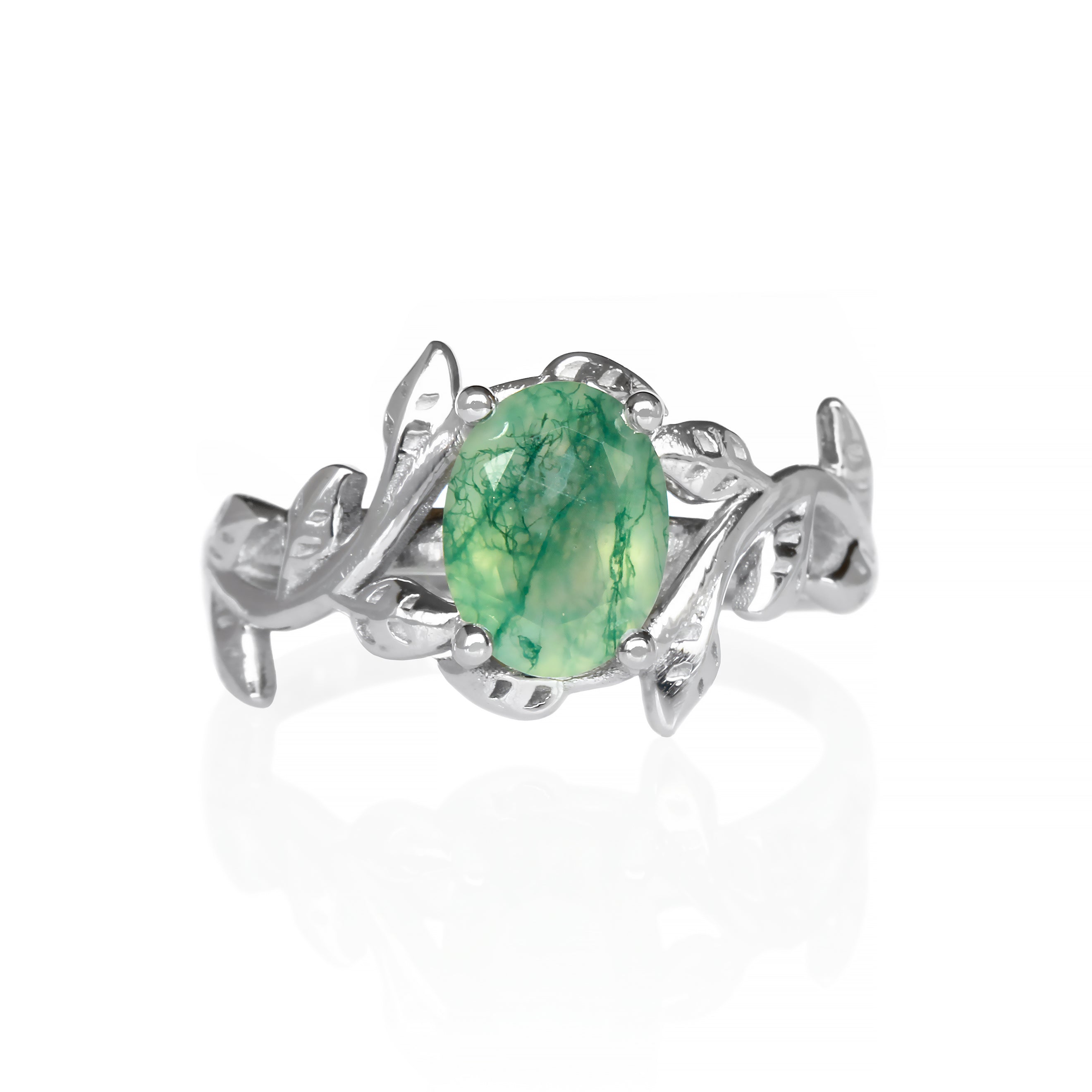 A delicate and ornate sterling silver ring featuring a 8x6mm oval moss agate center stone on a white background. The moss agate stone displays a unique pattern of green dendritic inclusions, resembling moss or lichen. The ring's intricate floral band is adorned with delicate leaf-like motifs, meticulously crafted with detailed veins and edges. Ideal for use as a promise ring, this nature-inspired piece showcases the beauty of natural gemstones and intricate craftsmanship.