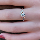 A product photo of moissanite ring in 9k white gold sitting on a woman's finger. The reflective round-cut moissanite sits in the centre, and a simple white gold band splits on either side of the jewel, holding it in place like the corners of an eye.