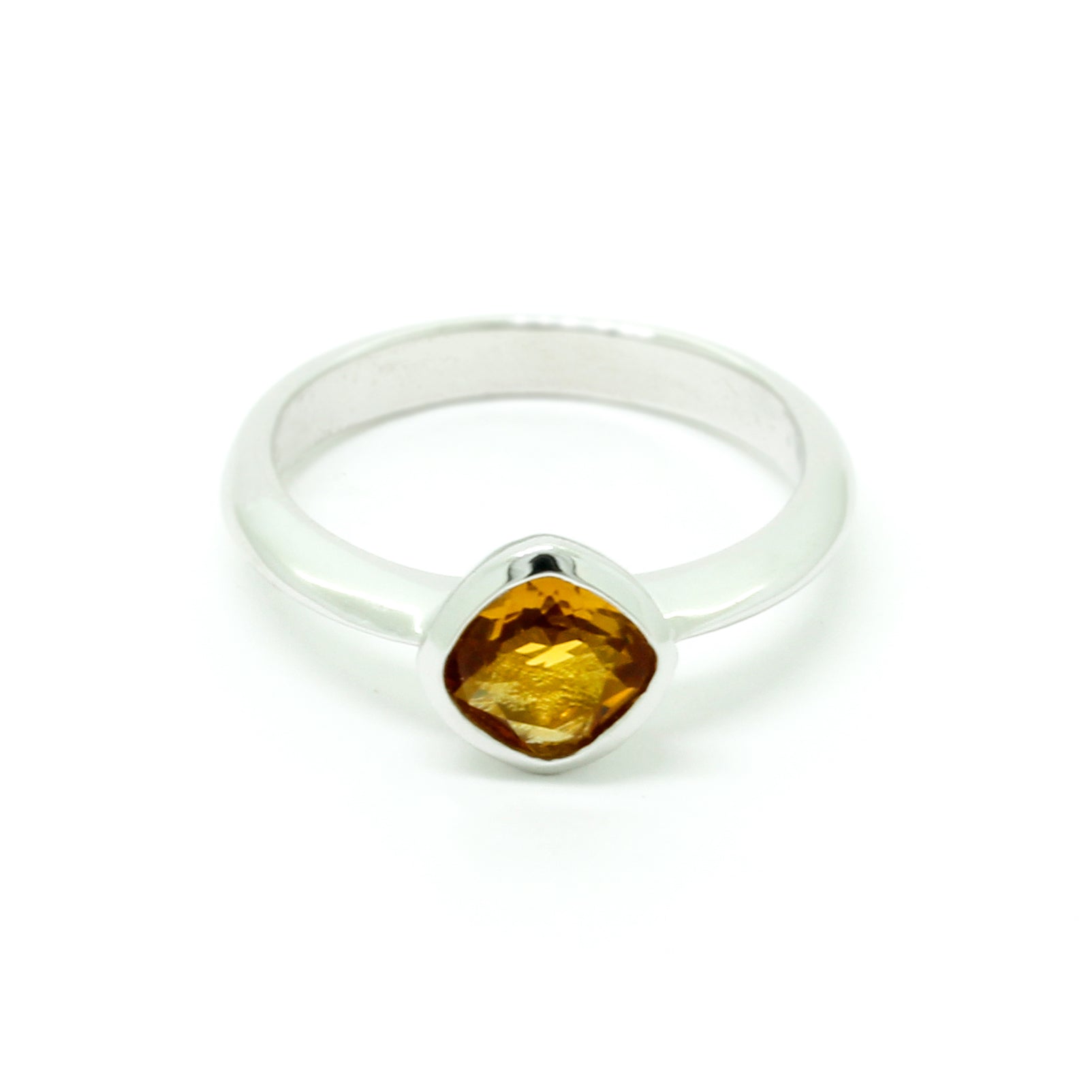 A product photo of a silver ring with a bezel-set citrine centre stone sitting on a white background. The silver band is simple and smooth, connecting on either side of a diagonally-oriented square cushion-cut citrine stone surrounded by a solid frame of silver. The citrine jewel is almost honey-coloured, reflecting a warm orangey yellow colour across its multi-faceted surface.