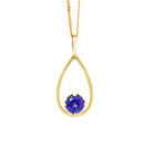 A product photo of a yellow gold tanzanite pendant suspended by a chain against a white background. The deep blue tanzanite stone, held in place by 4 claws, sits at the bottom of a slim, teardrop-shaped frame of yellow gold, and reflects violet blue and indigo colours from its many edges.