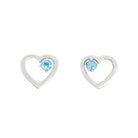 A product photo of two silver heart-shaped stud earrings sitting on a white background. A delicate, 2.5mm blue topaz stone is nestled in the top right corner of each heart-shaped frame.