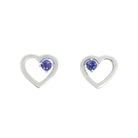 A product photo of two silver heart-shaped stud earrings sitting on a white background. A delicate, 2.5mm round violet-blue tanzanite stone is nestled in the top right corner of each heart-shaped frame.