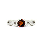 A product photo of an ornate silver ring with a garnet centre stone sitting on a white background. The silver band splits halfway along its length, becoming twisting and serpentine in appearance before meeting on either side of the deep red 5mm stone, which is held in place by 4 silver claws.