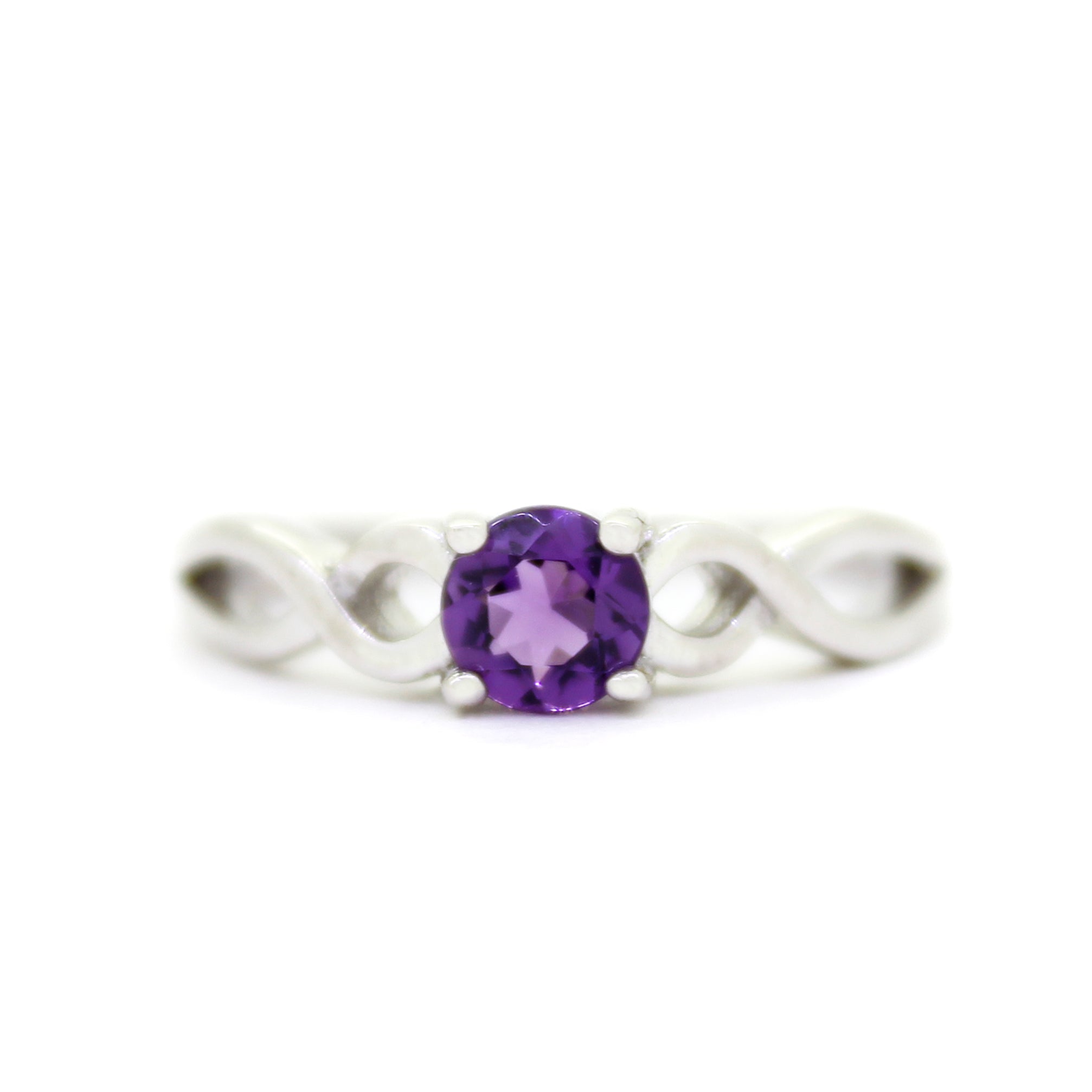 A product photo of an ornate silver ring with an amethyst centre stone sitting on a white background. The silver band splits halfway along its length, becoming twisting and serpentine in appearance before meeting on either side of the dazzling deep purple 5mm stone, which is held in place by 4 silver claws.