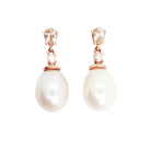 A product photo of a pair of ornate pearl drop stud earrings in rose gold suspended over a white background. The pearls are large and creamy white, with one small diamond followed by a pear-shaped pink morganite on each piece linking them to the back of the golden stud.