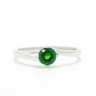 A product photo of a curved-band 9k white gold solitaire ring with a verdant-green tsavorite centre stone sitting on a white background. The green gemstone colour be a good emerald substitute.