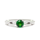 A product photo of an ornate white gold ring with a tsavorite centre stone sitting on a white background. The band splits halfway along its length, becoming twisting and serpentine in appearance before meeting on either side of the deep 5mm round tsavorite, which is held in place by 4 silver claws.  The green gemstone colour be a good emerald substitute.