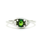 A product photo of a mystical tourmaline and diamond fantasy ring in solid 9k white gold on a white background. The deep, verdant-green tourmaline is held in place by 4 claws and reflects light off of its many facets, while the diamonds on either side are held by 3 each. The smooth white gold band curves elegantly, meeting at the top and bottom of the tourmaline and diamond arrangement. The green gemstone colour would be a good emerald substitute.