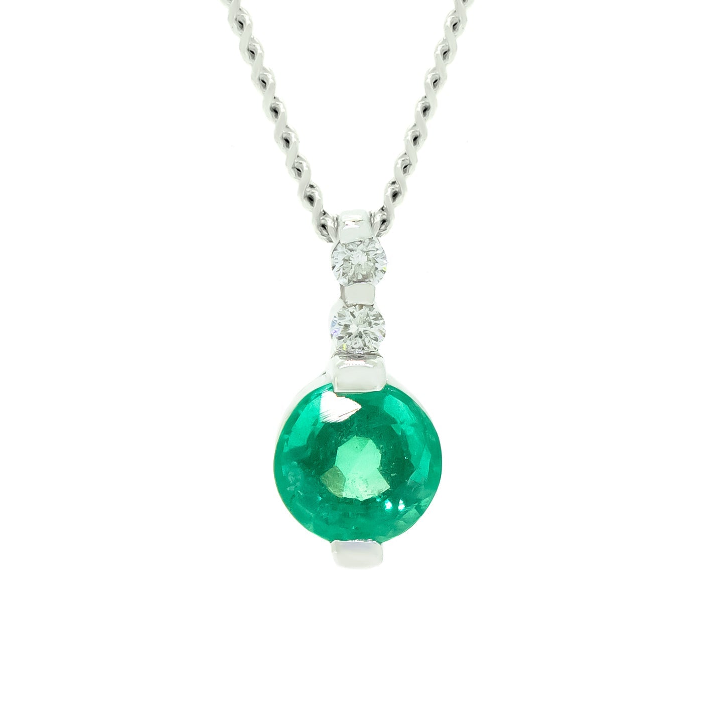 A product photo of a white gold emerald pendant sitting against a white background. The fine emerald stone is held in place by 2 claws at its top and bottom, with a two white diamonds connecting the stone to the rest of the pendant.