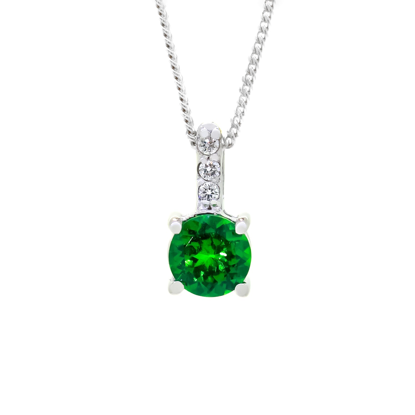 A product photo of a pair of a white gold tsavorite pendant suspended against a white background. The simple circle-cut stone are contrasted by the white diamond trio protruding in a straight line above it, encased in white gold.