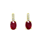 A product photo of a pair of yellow gold ruby earrings sitting against a white background. The simple oval-cut stones are contrasted by the white diamond trio protruding in a straight line above each burgundy magenta stone, encased in yellow gold.