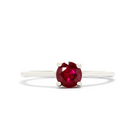 A product photo of a white gold ruby solitaire ring sitting on a white background. The band is smooth and simple, with the centre stone held in place by 4 small claws. The deep magenta ruby stone reflects sanguine hues from its many edges.