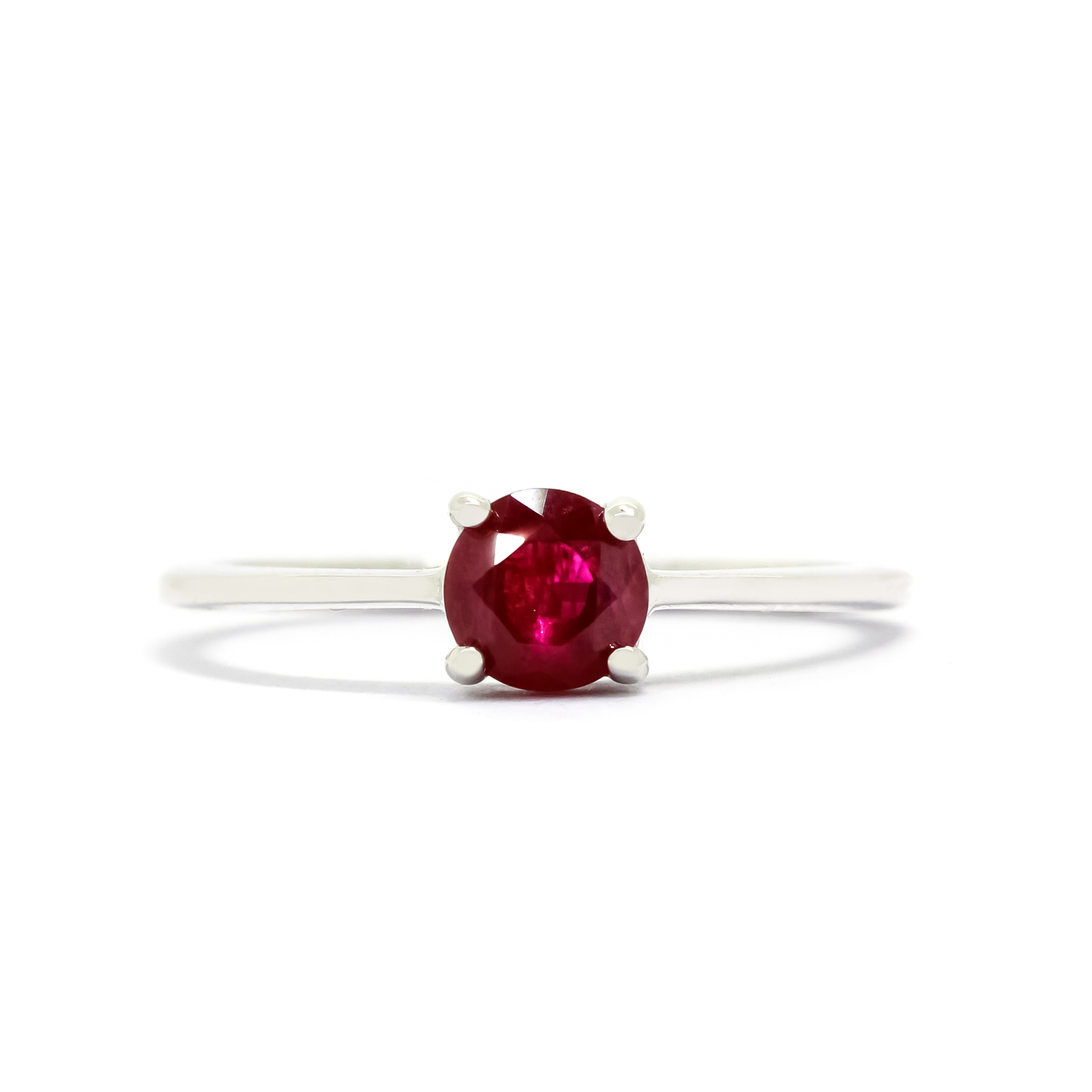 A product photo of a white gold ruby solitaire ring sitting on a white background. The band is smooth and simple, with the centre stone held in place by 4 small claws. The deep magenta ruby stone reflects sanguine hues from its many edges.